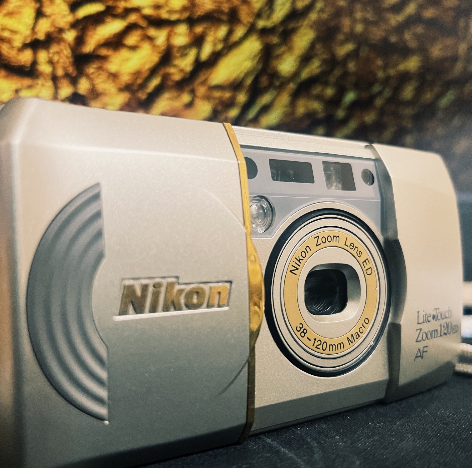 Photo of a partially opened Nikon Zoom 120 Edition Camera on a gold wrinkled background.